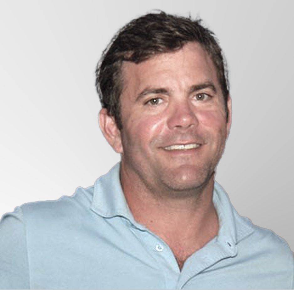 A man with short brown hair smiles at the camera. He is wearing a light blue collared shirt and is standing in front of a light gray gradient background.
