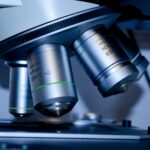 Close-up of the objective lenses of a microscope, showing three metal lenses labeled with magnification levels above a microscope stage—a vital tool in research supported by the Synovial Sarcoma Foundation.
