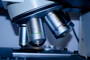 Close-up of the objective lenses of a microscope, showing three metal lenses labeled with magnification levels above a microscope stage—a vital tool in research supported by the Synovial Sarcoma Foundation.