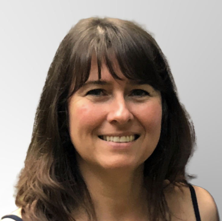 A woman with long brown hair and bangs smiles at the camera. She is wearing a dark top and is posed in front of a light gray, gradient background.