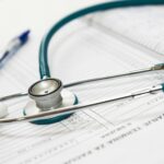 A stethoscope and a blue pen resting on top of a medical chart with patient information and handwritten notes.