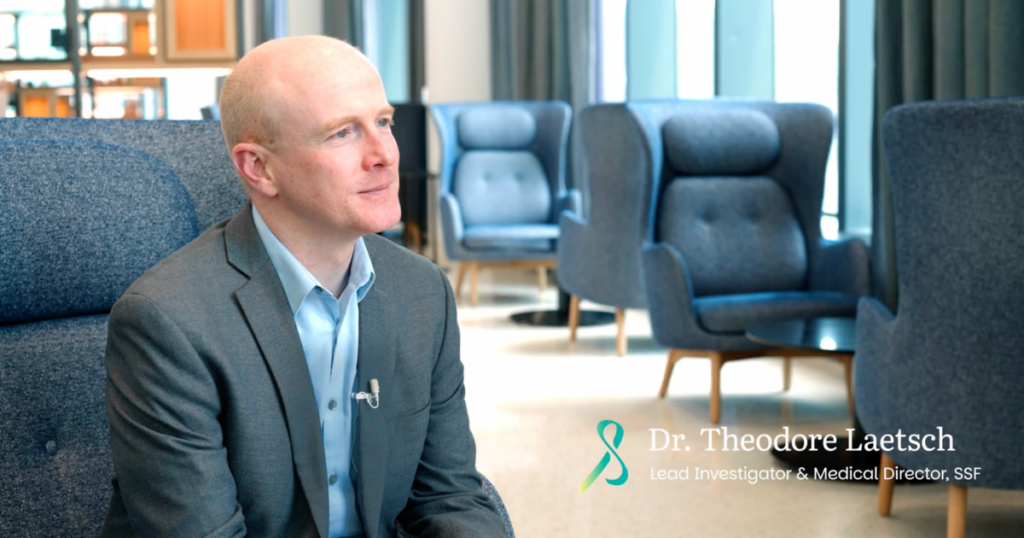 A man in a gray suit sits in a modern, well-lit office lounge. Text on the image reads: "Dr. Theodore Laetsch, Lead Investigator & Medical Director, SSF." Blue chairs and large windows are in the background.