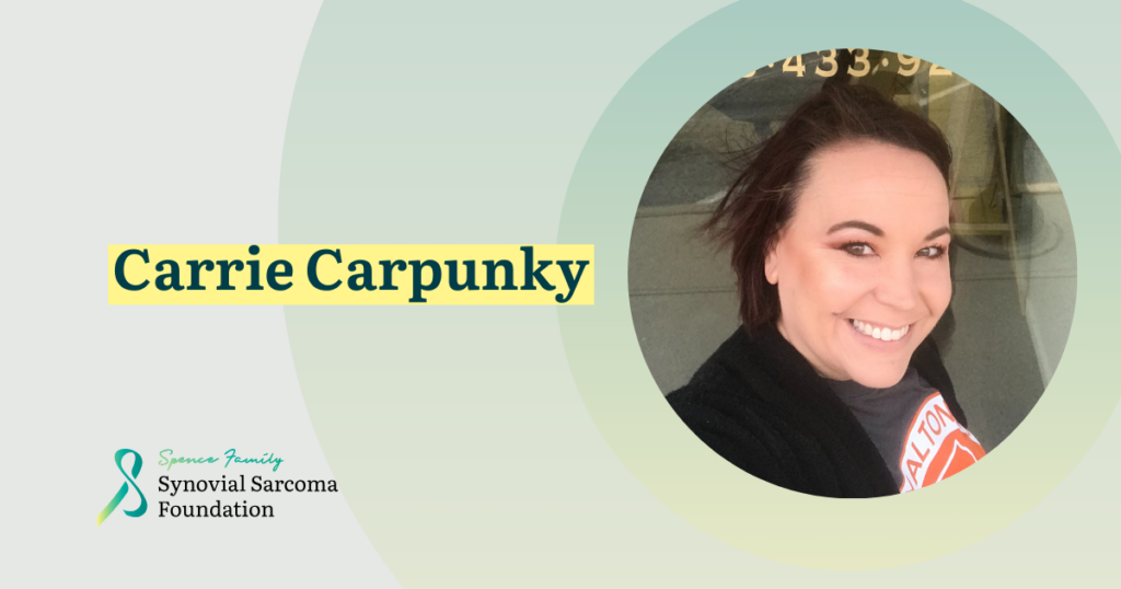 A smiling woman with short dark hair and a black shirt takes a selfie. Text reads "Carrie Carpunky." The Synovial Sarcoma Foundation’s name and logo appear in the bottom left corner.