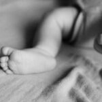 Black and white photo of a baby's legs and feet resting on a soft blanket, with the focus on the feet and toes. The background and upper body are blurred.