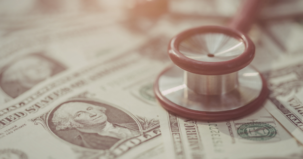 A stethoscope rests on several one-dollar bills, symbolizing the connection between healthcare and financial costs. The focus is on the stethoscope and a bill featuring George Washington.