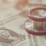 A stethoscope rests on several one-dollar bills, symbolizing the connection between healthcare and financial costs. The focus is on the stethoscope and a bill featuring George Washington.