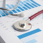 A stethoscope rests on printed charts and graphs with blue bars and lines, representing medical or healthcare statistics and data analysis.
